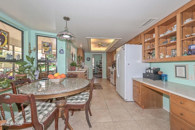 kitchen with visible vents, freestanding refrigerator, brown cabinetry, light countertops, and built in study area