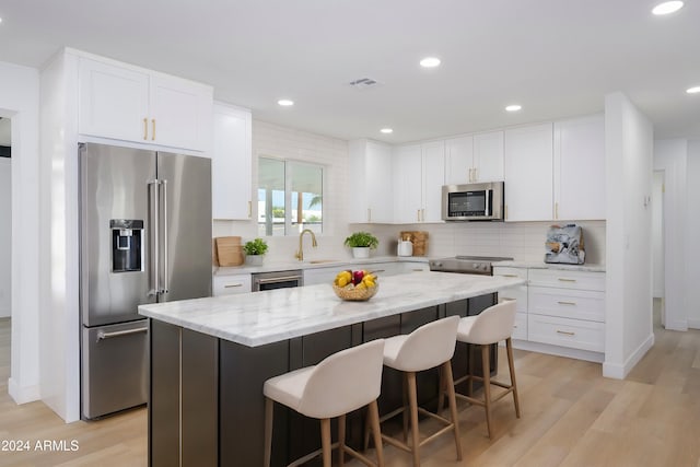 kitchen featuring white cabinetry, light stone counters, decorative backsplash, a kitchen island, and appliances with stainless steel finishes