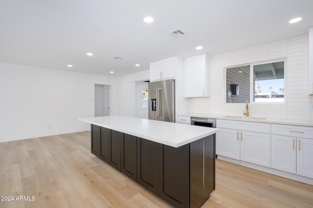 kitchen with decorative backsplash, stainless steel appliances, sink, a center island, and white cabinetry