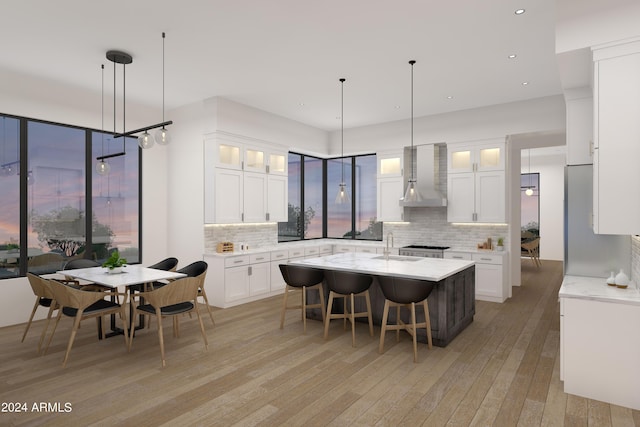 kitchen featuring a breakfast bar, light wood-style floors, white cabinets, a kitchen island with sink, and wall chimney exhaust hood