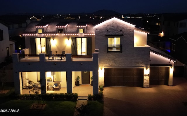 view of front of house with a garage, a balcony, concrete driveway, stone siding, and stucco siding
