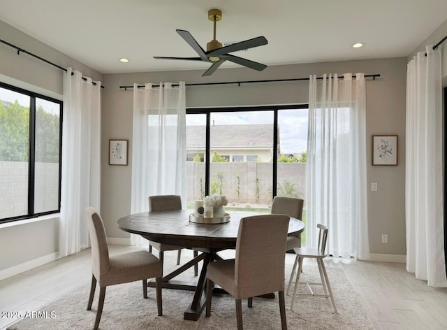 dining area featuring light wood-style floors, baseboards, ceiling fan, and a wealth of natural light
