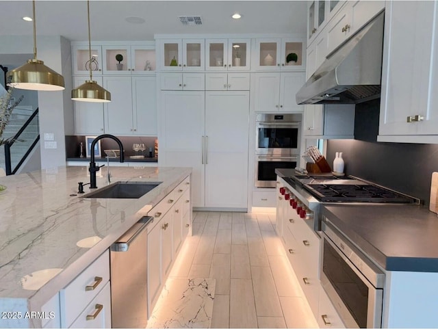 kitchen with a sink, stainless steel appliances, under cabinet range hood, visible vents, and pendant lighting