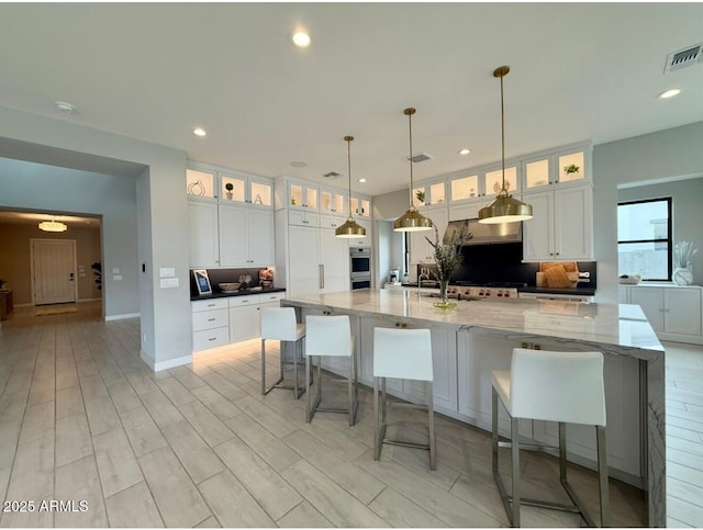 kitchen featuring white cabinets, recessed lighting, a large island with sink, backsplash, and visible vents