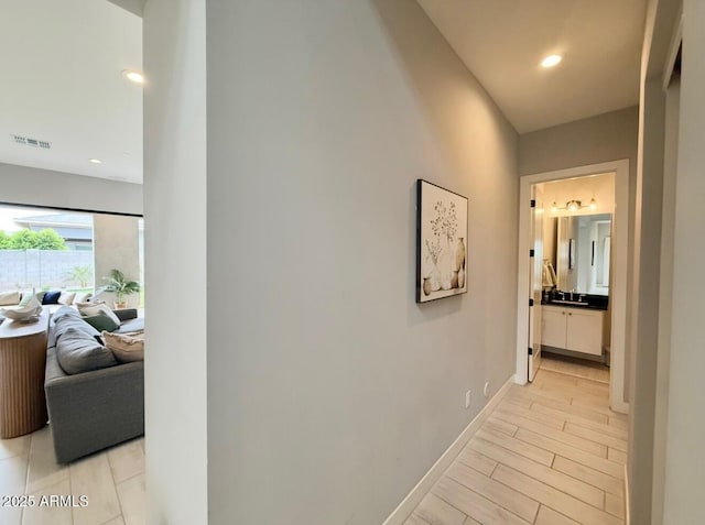 hallway featuring visible vents, baseboards, light wood-style floors, recessed lighting, and a sink