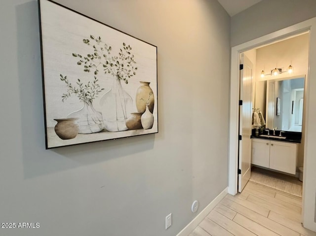 hall featuring a sink, baseboards, and light wood-type flooring