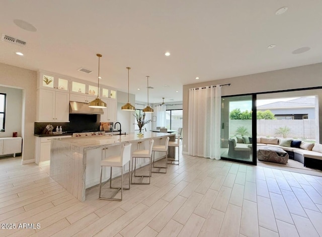 kitchen with a large island, visible vents, a sink, open floor plan, and under cabinet range hood