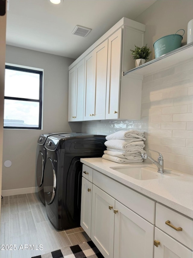 washroom with visible vents, baseboards, separate washer and dryer, a sink, and cabinet space