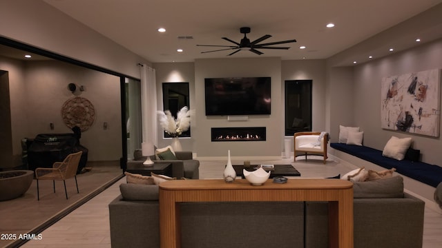living area with recessed lighting, a ceiling fan, light wood finished floors, and a warm lit fireplace