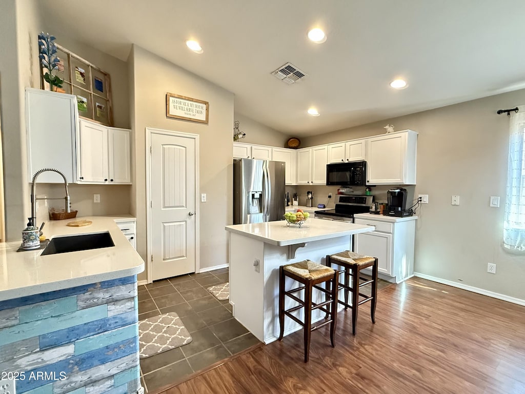 45499 W Sky Ln, Maricopa, AZ 85139 - kitchen featuring appliances with stainless steel finishes, vaulted ceiling, a breakfast bar area, a kitchen island, and white cabinetry