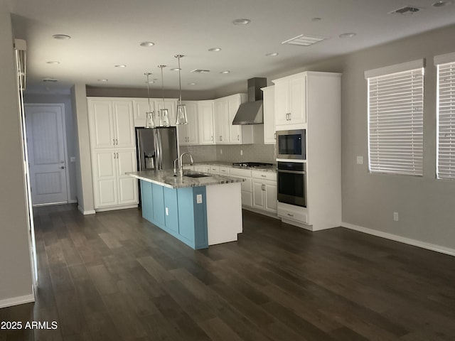 kitchen featuring pendant lighting, a center island with sink, wall chimney exhaust hood, white cabinetry, and stainless steel appliances