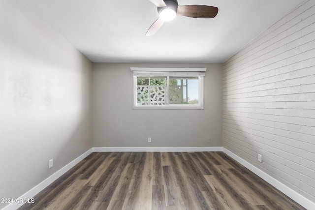 unfurnished room with ceiling fan, brick wall, and dark hardwood / wood-style floors