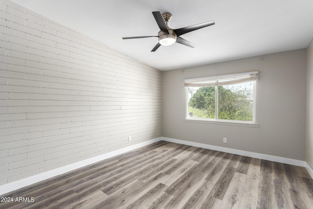 unfurnished room featuring lofted ceiling, hardwood / wood-style floors, ceiling fan, and brick wall