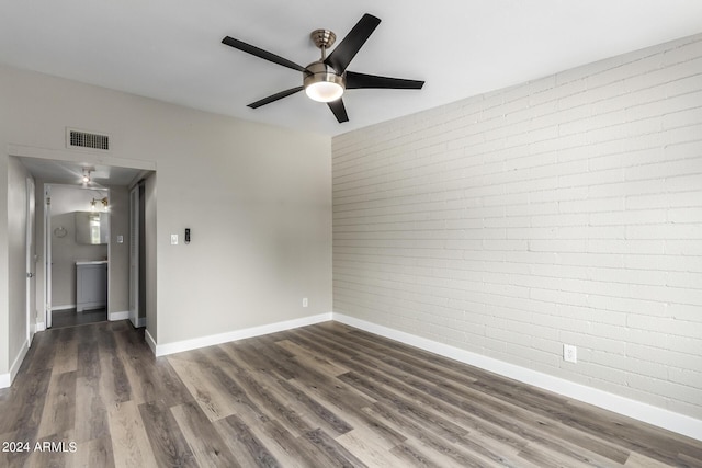 spare room featuring dark hardwood / wood-style flooring, ceiling fan, and brick wall