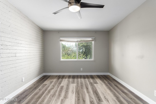 unfurnished room featuring ceiling fan, brick wall, and light hardwood / wood-style floors