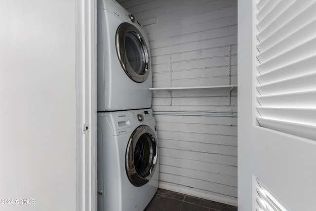 laundry room with stacked washer / drying machine and dark tile patterned flooring