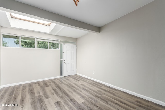 unfurnished room featuring a skylight, beamed ceiling, and light wood-type flooring