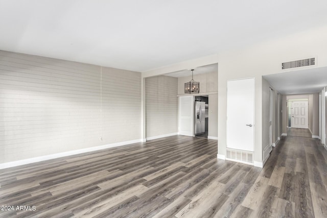 unfurnished living room with brick wall, a chandelier, and dark hardwood / wood-style flooring