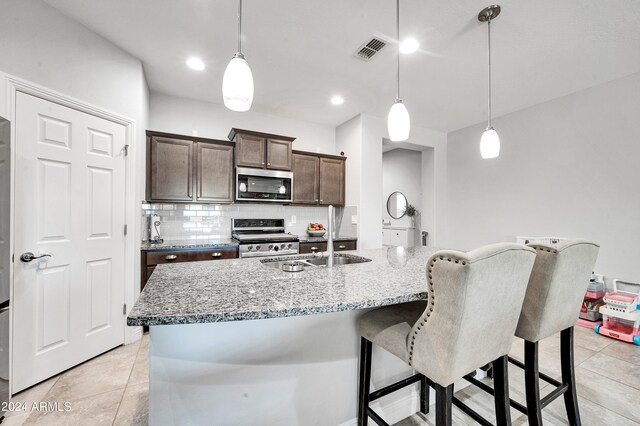 kitchen featuring dark brown cabinetry, decorative light fixtures, an island with sink, and stainless steel appliances