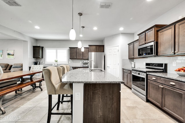 kitchen featuring light stone countertops, an island with sink, stainless steel appliances, and decorative light fixtures