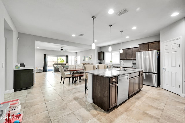 kitchen with ceiling fan, hanging light fixtures, sink, a center island with sink, and stainless steel appliances