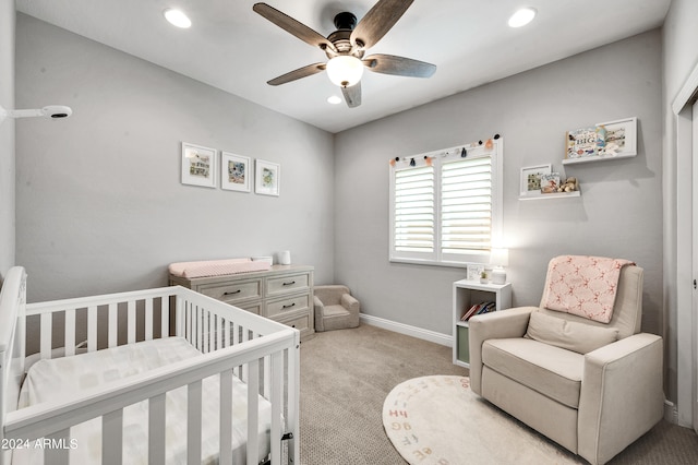 carpeted bedroom featuring ceiling fan and a nursery area