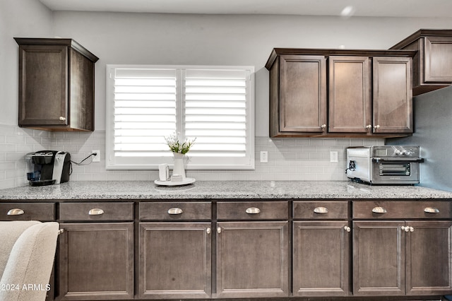 kitchen with dark brown cabinetry, decorative backsplash, and light stone counters