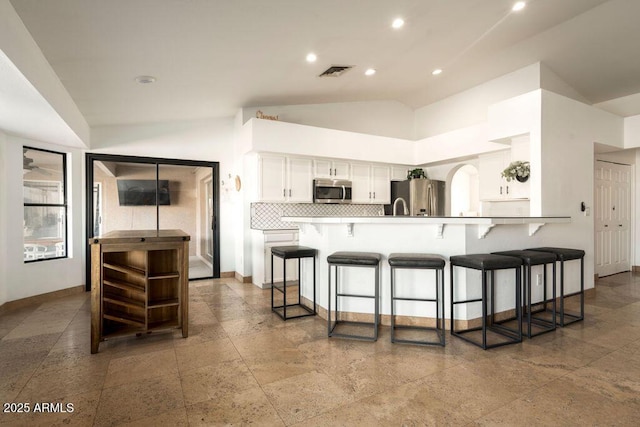 kitchen featuring appliances with stainless steel finishes, white cabinetry, a breakfast bar area, backsplash, and kitchen peninsula