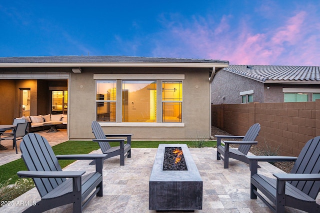 back house at dusk with an outdoor living space with a fire pit and a patio