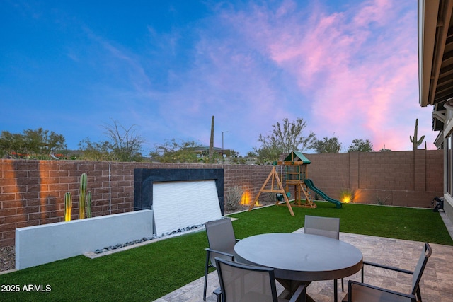 patio terrace at dusk featuring a yard and a playground