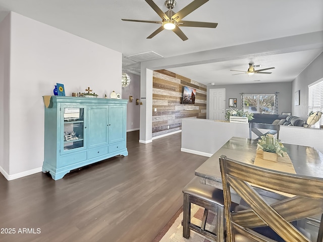 dining room with an accent wall, dark wood-type flooring, a ceiling fan, wood walls, and baseboards