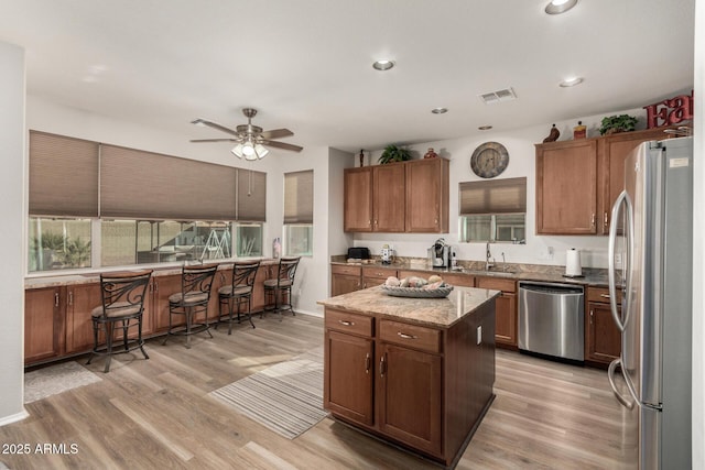 kitchen with ceiling fan, sink, light hardwood / wood-style flooring, a kitchen island, and appliances with stainless steel finishes