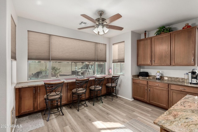 kitchen with light stone countertops, light wood-type flooring, and ceiling fan