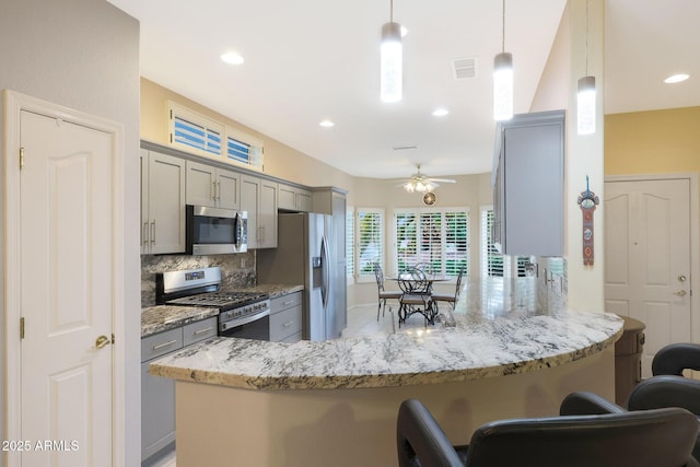 kitchen featuring a kitchen bar, appliances with stainless steel finishes, gray cabinets, kitchen peninsula, and backsplash