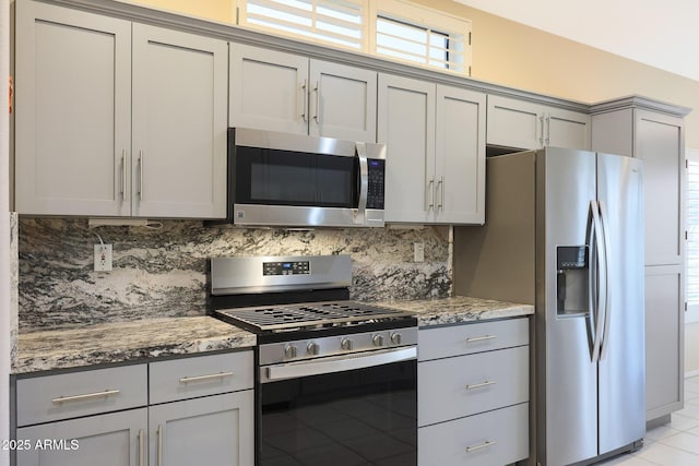 kitchen with stone countertops, light tile patterned floors, gray cabinets, stainless steel appliances, and decorative backsplash