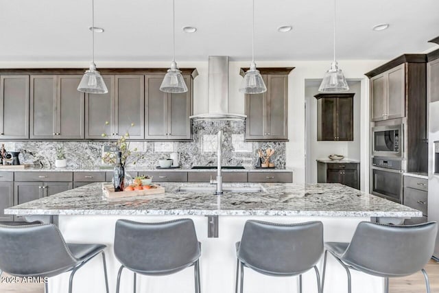 kitchen with pendant lighting, wall chimney exhaust hood, and an island with sink