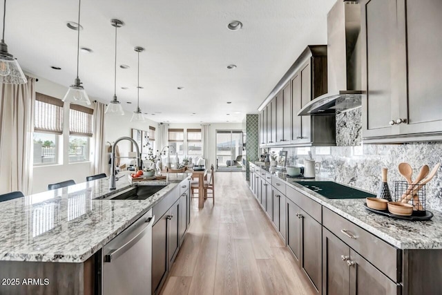 kitchen featuring decorative light fixtures, wall chimney range hood, a spacious island, stainless steel dishwasher, and sink