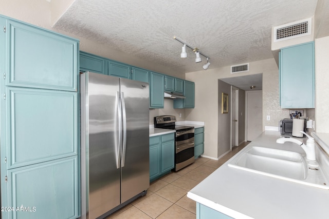 kitchen featuring blue cabinets, rail lighting, sink, light tile patterned flooring, and stainless steel appliances