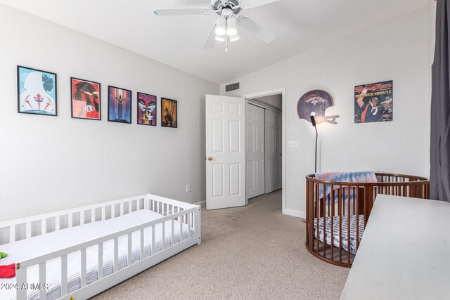 carpeted bedroom with ceiling fan, a crib, and a closet