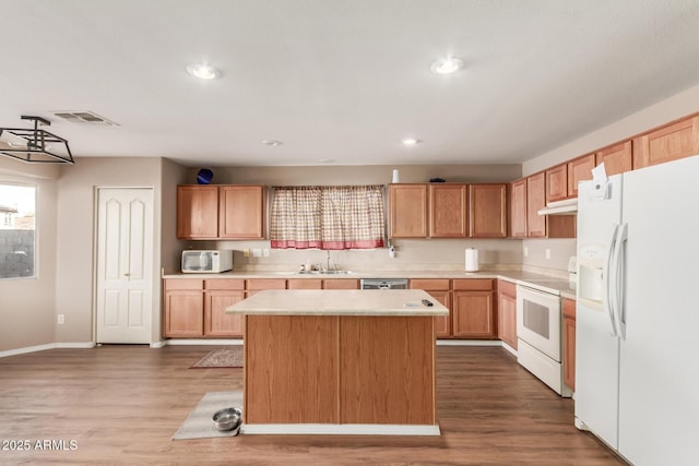 kitchen featuring visible vents, under cabinet range hood, light countertops, white appliances, and a sink