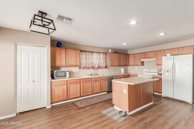 kitchen featuring visible vents, under cabinet range hood, light countertops, white appliances, and a sink