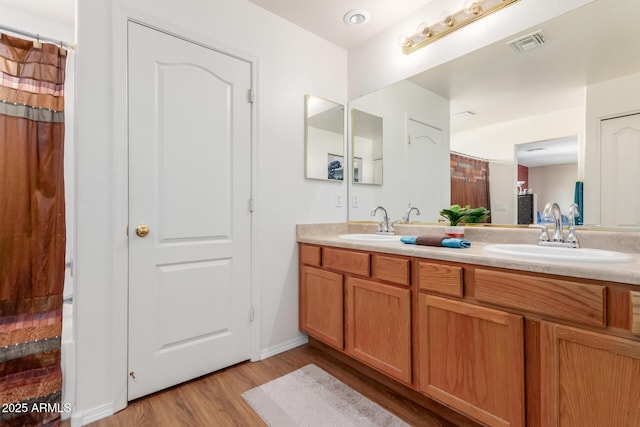 full bathroom with a sink, visible vents, wood finished floors, and double vanity