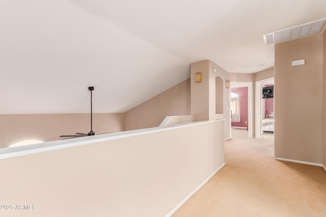 hallway featuring lofted ceiling, visible vents, baseboards, and light carpet