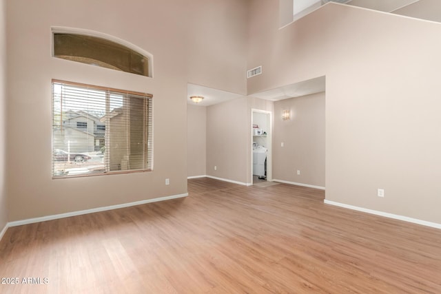 empty room featuring visible vents, light wood-style flooring, baseboards, and a towering ceiling