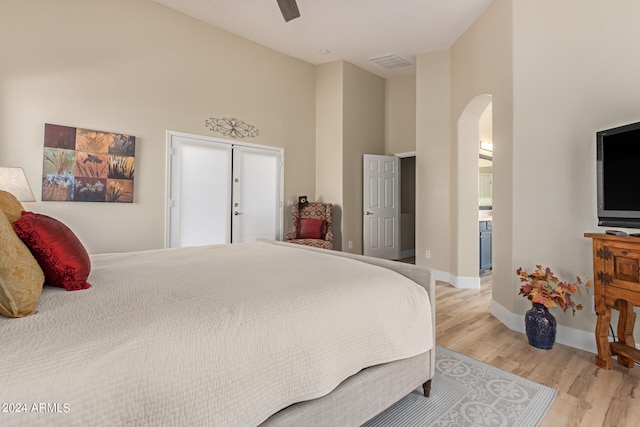 bedroom featuring light hardwood / wood-style flooring, ceiling fan, connected bathroom, and a high ceiling