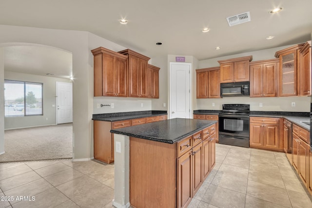 kitchen featuring dark stone countertops, a center island, light carpet, and black appliances