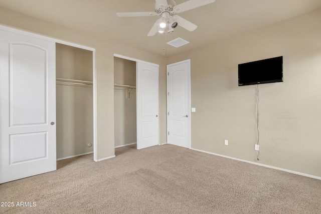 unfurnished bedroom featuring carpet flooring, multiple closets, and ceiling fan