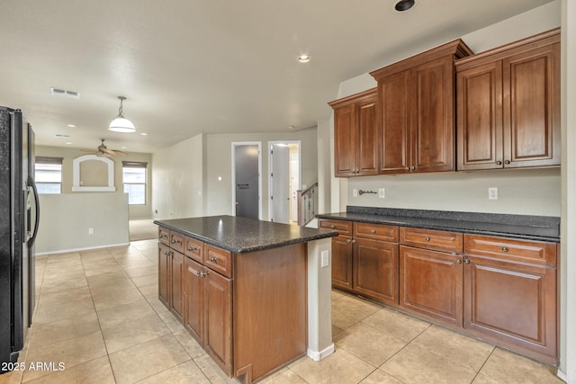 kitchen with a center island, black fridge, light tile patterned floors, dark stone countertops, and ceiling fan