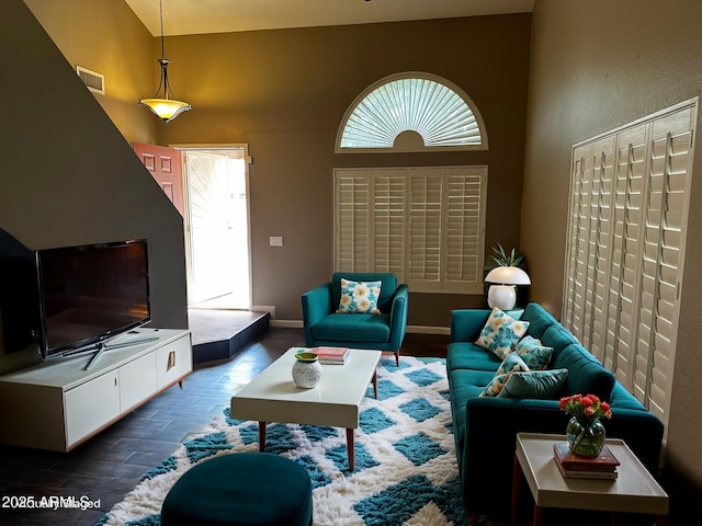 living area with visible vents, baseboards, wood finished floors, and a towering ceiling