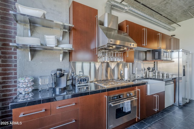 kitchen featuring dark tile patterned floors, a sink, stainless steel appliances, wall chimney range hood, and decorative backsplash